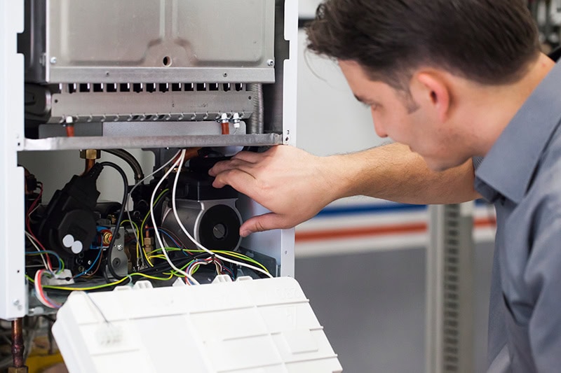 4 Important Heat Pump Maintenance Tips. A technician working on a heat pump.